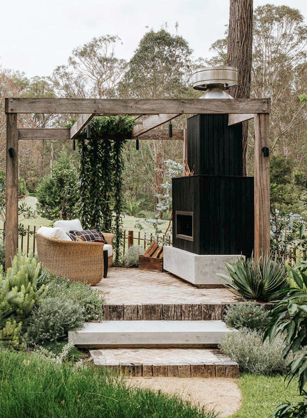 Outdoor living space with wooden pergola, lounge chair, and barbecue/fireplace area.
