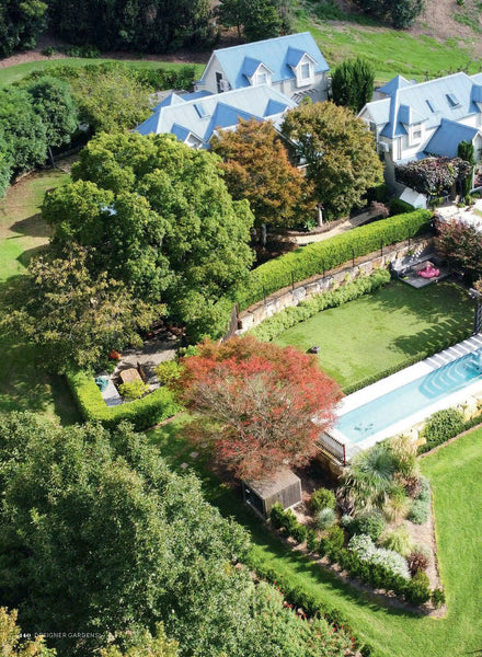 Aerial view of a large house with a pool surrounded by trees and gardens.